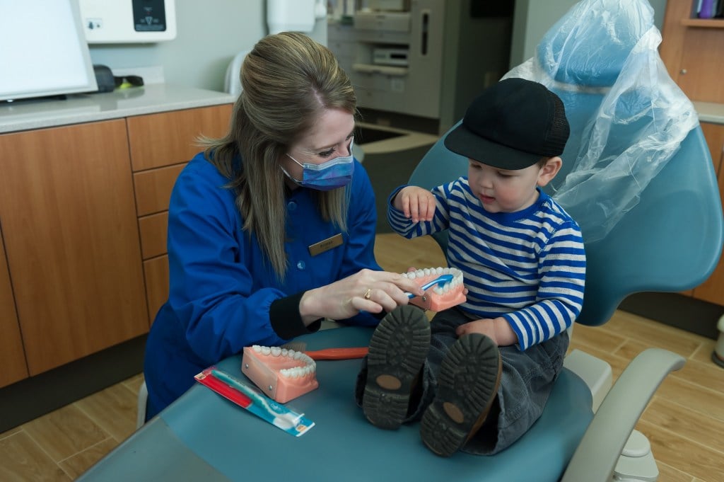 One of the dental staff members showing a young child how to brush their teeth